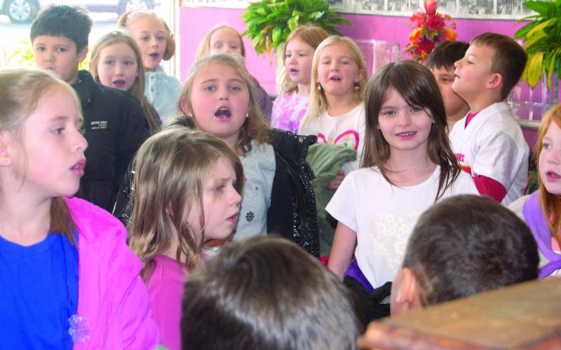 Second grade students in the classes of Becky Crystal and Rylee Crain sang, “We Wish You a Merry Christmas,” and other holiday tunes at various businesses around the Square December 17. News Report photo by Shawn Churchill.