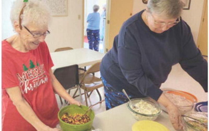 At the December 12 Bunco games, members held a Christmas potluck and pajama party. Barbara Poor and Cathy Andersen were helping arrange the dishes on the table for the luncheon.