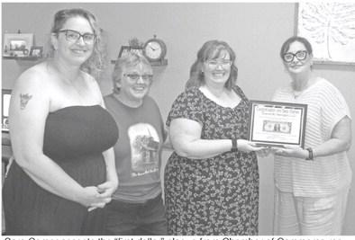 Sara Comer accepts the “first dollar” plaque from Chamber of Commerce representative Rebecca Spooner (far right).