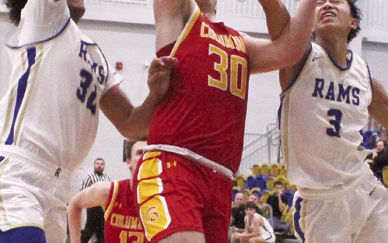 Titan Senior, Brett Hamilton, goes in for two points between Ram Senior, Jamey Richardson and junior, Zach Feldkamp in the final minutes of the, 59-48, Columbus win in Riverton, Friday.