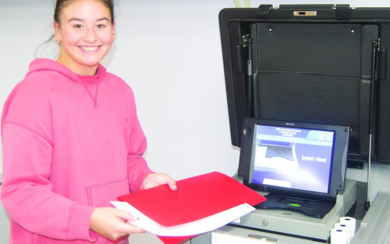 Poll worker Jailyn Rodriguez explains to the voter how to insert their ballot into the vote counting machine during Tuesday’s election. She was working in the Salamanca Township poll at the Kansas State Research and Extension office.