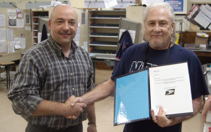 Columbus Postmaster Tyler Speer presents retiring Ron Steele with a certificate of appreciation for his 14 years as custodian.