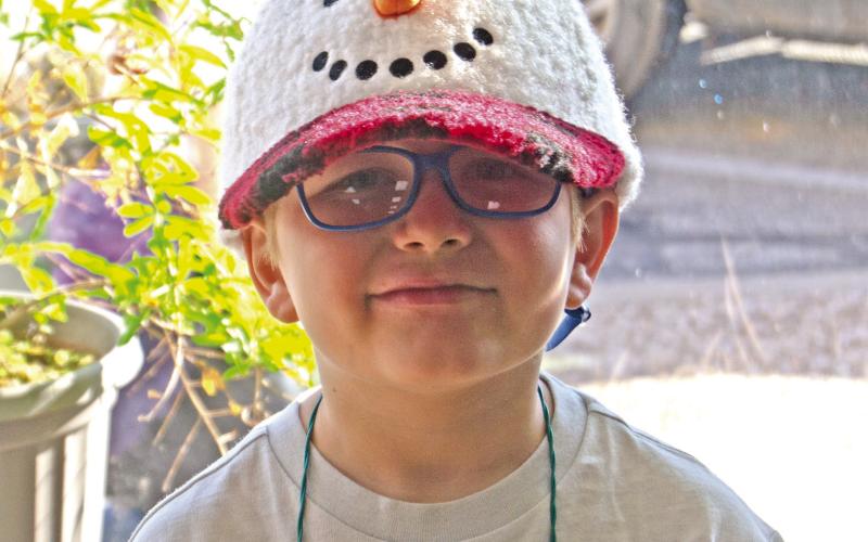 The weather might have been warm, but Manny Napier sported his snowman cap while the second grade classes sang carols around the square before Christmas break. News Report photo by Shawn Churchill.