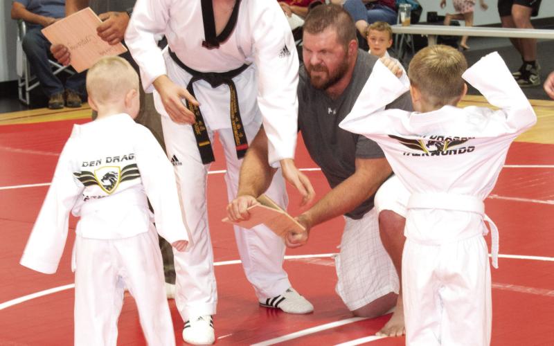Student Duke Kelly listens as Master Vigil explains the kick required to break the board while student Kellian Mclean looks on. Dukes father is holding the board.