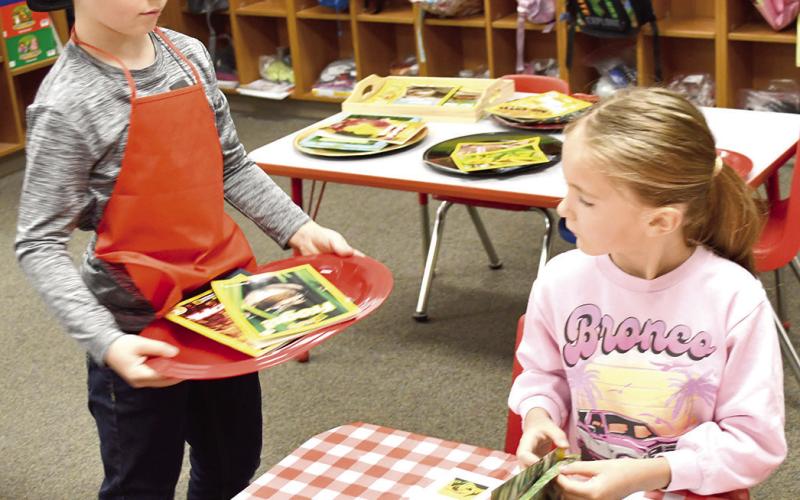 Brooks Crain served a book to Aarolynn Elmore during the Kindergarten book tasting event at Park Elementary for Read Across America Week. First graders assisted kindergarteners in selecting and reading the different books. News Report photo by Tanya Woolsey.