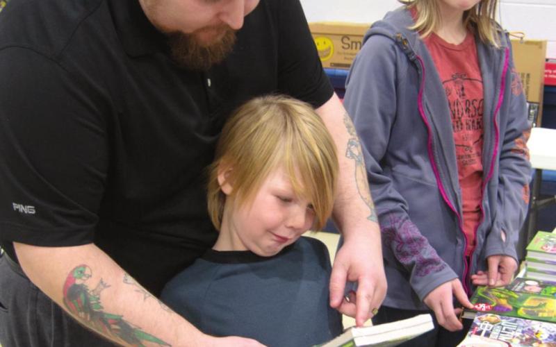 Family Night at Spring Grove Primary School was a huge success in the community, offering a book fair and several activities for the attending families. Derrick January stops to show his children, Arkham January and Jaden January, some of the interesting titles he found as they shop. Photo by Jacob Spencer.