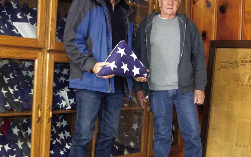Standing before a cabinet filled with flags belonging to families of veterans from Weir. Larry Spahn, representing the American Legion and Milt Alexander representing the Weir Civic Club are seeking to give veteran’s flags to their family members.