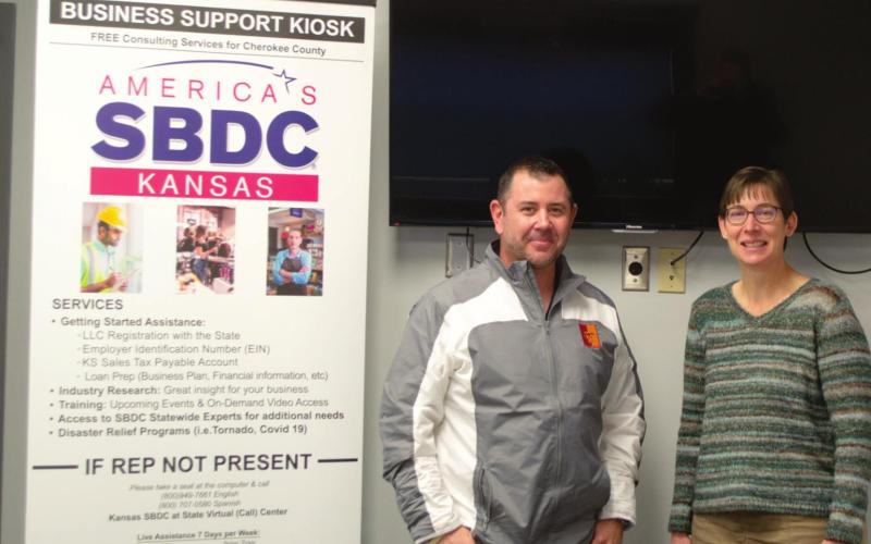 Chris Pennington, the Kansas SBDC State Virtual Center Director, poses with Janet Miller, the Cherokee County Economic Development Director, at the center in Columbus. A kiosk that hangs above the pair offers virtual assistance to local entrepreneurs and established business owners in addition to the pair’s expertise on a variety of financial topics. Photo by Jacob Spencer.