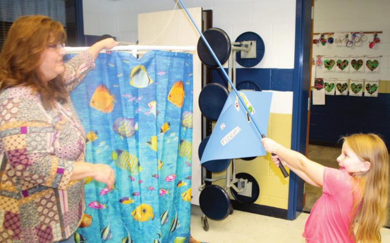 Riverton Elementary Student Lilly Linam plays a fishing game in Riverton Elementary School’s cafeteria. Valori Stone lady holds a fishing pole over an ocean-themed curtain to snag a sweet prize of candy and toys on the other side. Photo by Jacob Spencer