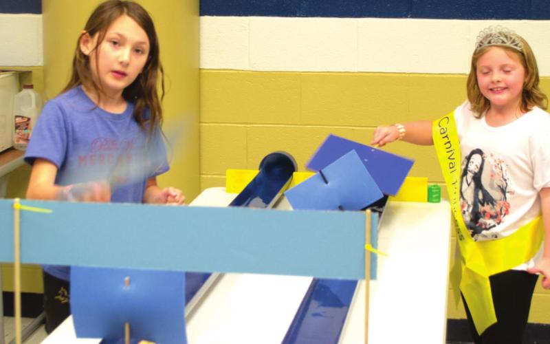 Riverton Elementary Students Anniston Huffman (left) and Arabella Friend (right) play a boat racing game in Riverton Elementary School’s cafeteria. Friend wears a sash after being nominated as the carnival’s princess for her ticket sales. Both girls wave fans at their boats to race them down individual tracks. Photo by Jacob Spencer