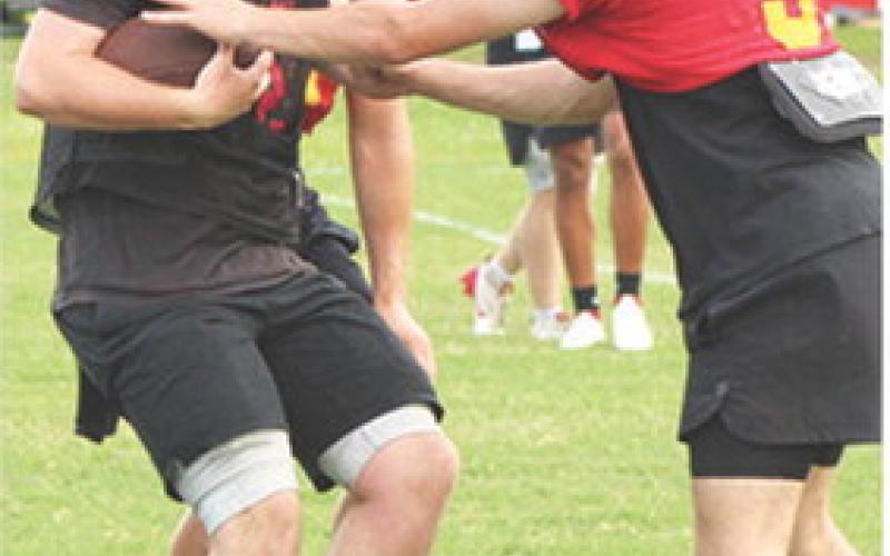 Columbus Titan Sophomore Quarterback, Cole Howard, takes a snap and begins his run against the Neodesha Defense during the Emporia State University Football Clinic, July 18, at the Central School Soccer Pitch. Right: Titan Senior Running Back, Jett Tanner is halted after a nice gain by the Labette County Defender. Cherryvale, Parsons, and Coffeyville were the additional three teams taking advantage of the tutelage of the Emporia State Staff.