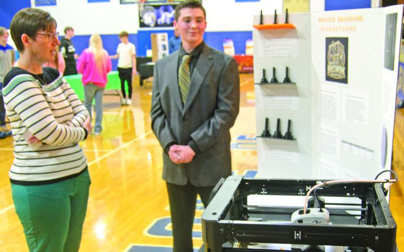 Winner of the first prize at the Cherokee County Entrepreneur Fair, Andrew Low, received the $1,500 prize. Judge Janet Miller discusses his project using a 3-D Printer. The printer was operating during the judging making brass instrument mouthpieces.