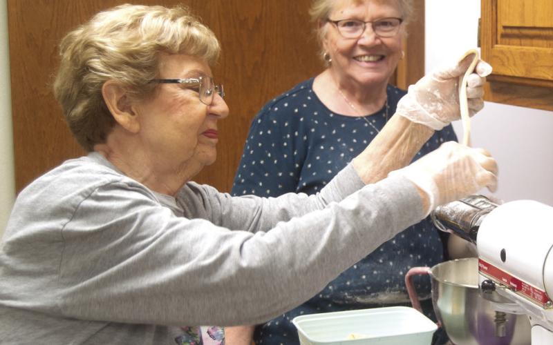 Mercy Auxiliary members gathered recently to make noodles for a fundraiser. Lucille McNemar was placing the dough into the cutter while Clara White looked on. Columbus News Report photo by Shawn Churchill.