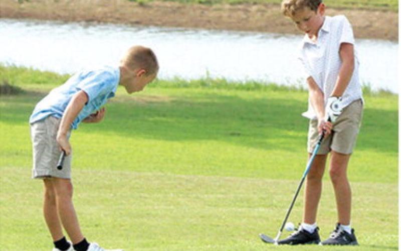 Jack Koons has a watchful eye in Hollis Havercamp’s chip shot during the Thursday junior golf clinic at the Brush Creek Golf Course. Lady Titan Sophomore, Cali Carpino and Titan Senior, Easton Long shared their talents and knowledge with the campers during the multi-week camp.