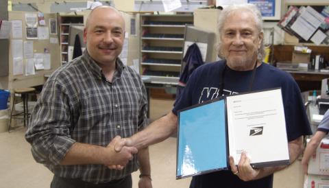 Columbus Postmaster Tyler Speer presents retiring Ron Steele with a certificate of appreciation for his 14 years as custodian.