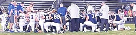 Players and coaches for the Riverton Rams and Galena Bulldogs Football Teams knelt and prayed together for Riverton Head Basketball Coach, Brandon Pate, following their CNC League game in Galena, Friday. Coach Pate’s wife, Paige Christiansen Pate teaches Spanish in both school districts. Galena won the contest, 42-24. Courtesy Photo.