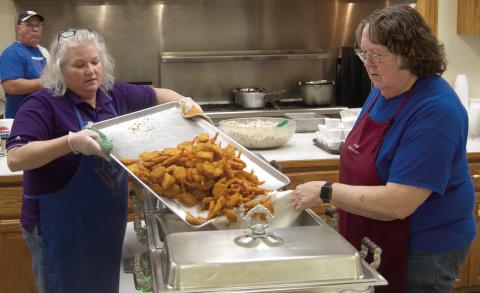 Rhonda Herrenbruck and Margie Wilson transfer the freshly cooked shrimp to the serving trays during the Friday night fish fry at St. Bridget’s. The event will continue until Easter.