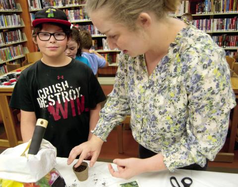 Tucker David watches as Cherokee County extension agent Kate Fluckiger puts seeds in a grow cup during the Garden Program for Kids at the Weir Library on Thursday. The youngsters were given soil and seeds and instructions on caring for the plants.