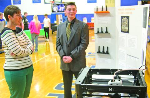 Winner of the first prize at the Cherokee County Entrepreneur Fair, Andrew Low, received the $1,500 prize. Judge Janet Miller discusses his project using a 3-D Printer. The printer was operating during the judging making brass instrument mouthpieces.