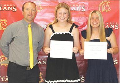Seniors, Trinity Green and Morgan Richards, received the Tom Goettel Scholarship in the amount of $1,000 each from USD 493 Staff Member, Jerry Smiley, during the 2026 Senior Assembly, May 15, at the Columbus Unified High School Gymnasium.