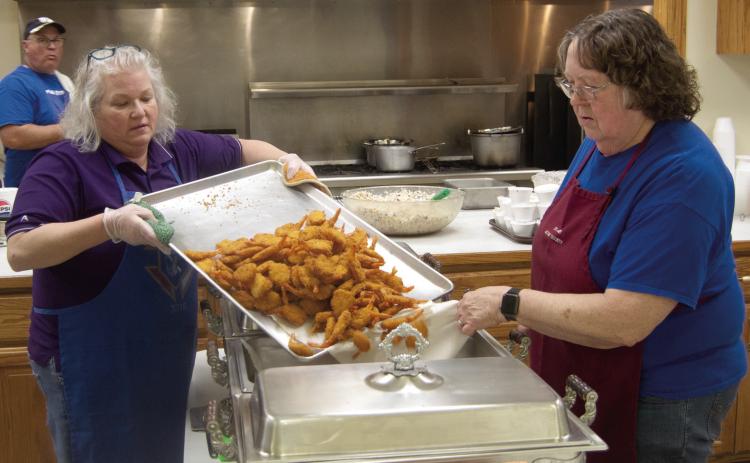 Rhonda Herrenbruck and Margie Wilson transfer the freshly cooked shrimp to the serving trays during the Friday night fish fry at St. Bridget’s. The event will continue until Easter.
