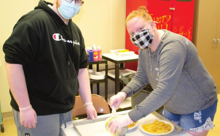 The third grade classes were assisted by high school students in their Read Across America program on Friday. The high school students were making apple pie while the Highland third graders were making pizza. Korbyn Martin and Livia Rooney put the apples in the pie shell crusts.