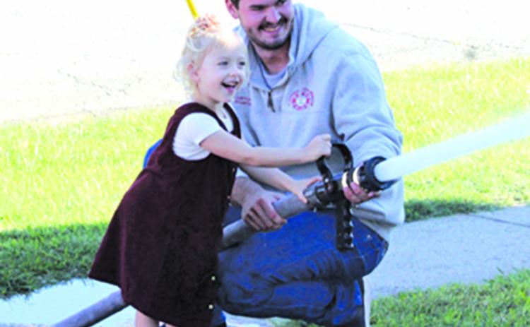 Columbus Firefighter Hunter Burton helps Eleanor Otto aim the fire hose during Fire Prevention Week.
