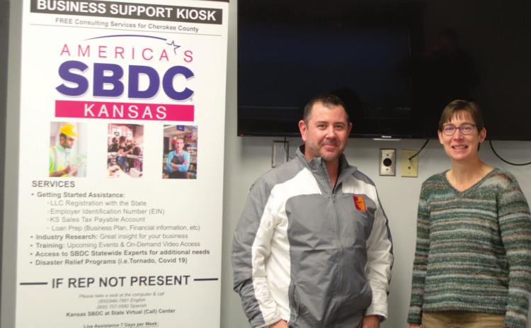 Chris Pennington, the Kansas SBDC State Virtual Center Director, poses with Janet Miller, the Cherokee County Economic Development Director, at the center in Columbus. A kiosk that hangs above the pair offers virtual assistance to local entrepreneurs and established business owners in addition to the pair’s expertise on a variety of financial topics. Photo by Jacob Spencer.