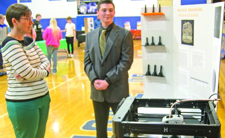 Winner of the first prize at the Cherokee County Entrepreneur Fair, Andrew Low, received the $1,500 prize. Judge Janet Miller discusses his project using a 3-D Printer. The printer was operating during the judging making brass instrument mouthpieces.